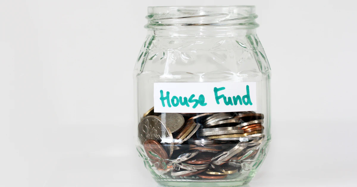 Coins in a glass savings jar labelled house fund, like a savings goal in the best budgeting apps