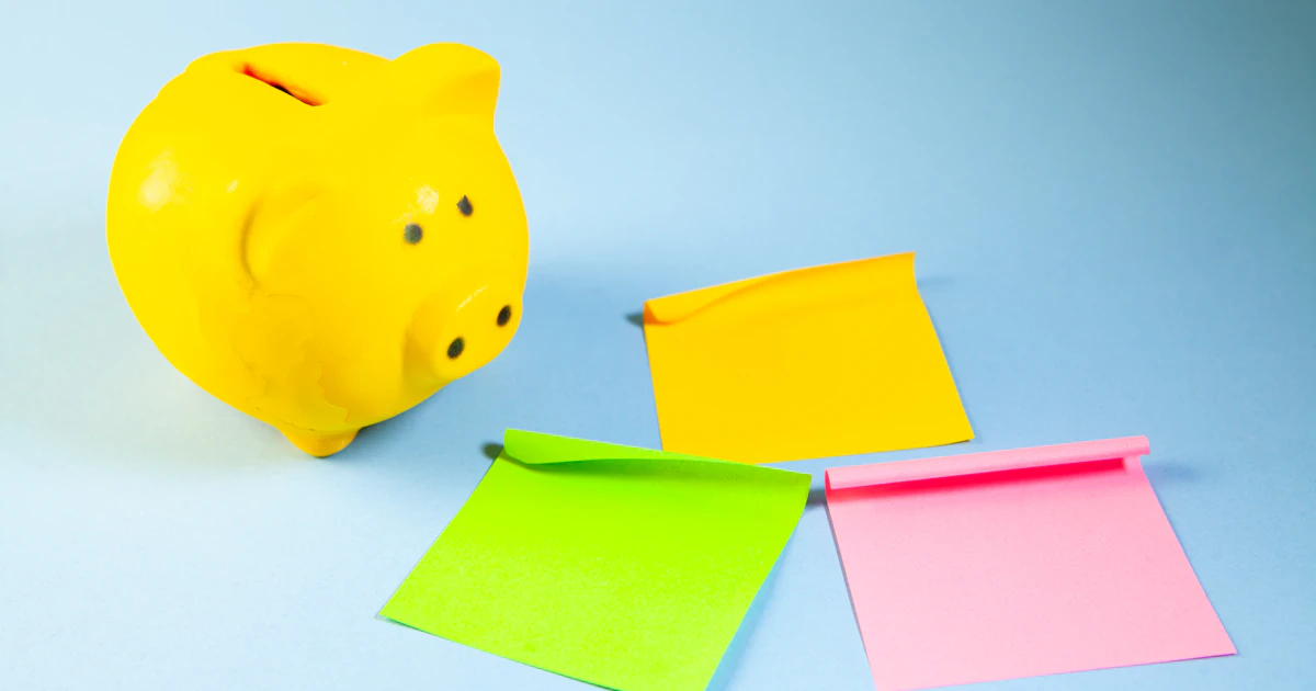 How to make money with AI: yellow piggy bank with colourful sticky notes on a blue background